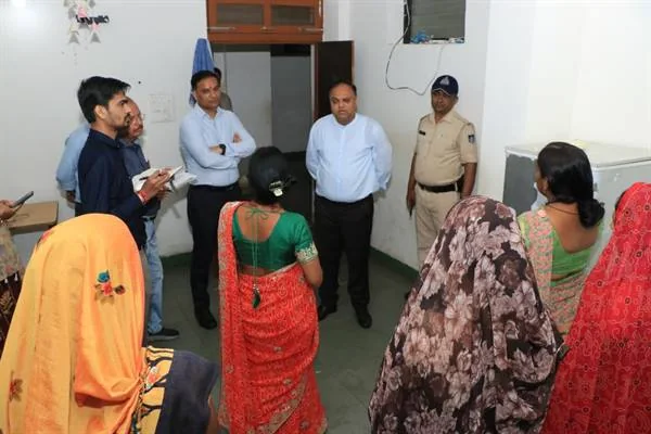 छात्रावास के एक कमरे में अधिकारियों से बातचीत करतीं महिलाएं, साथ में पुलिसकर्मी और अन्य कर्मचारी